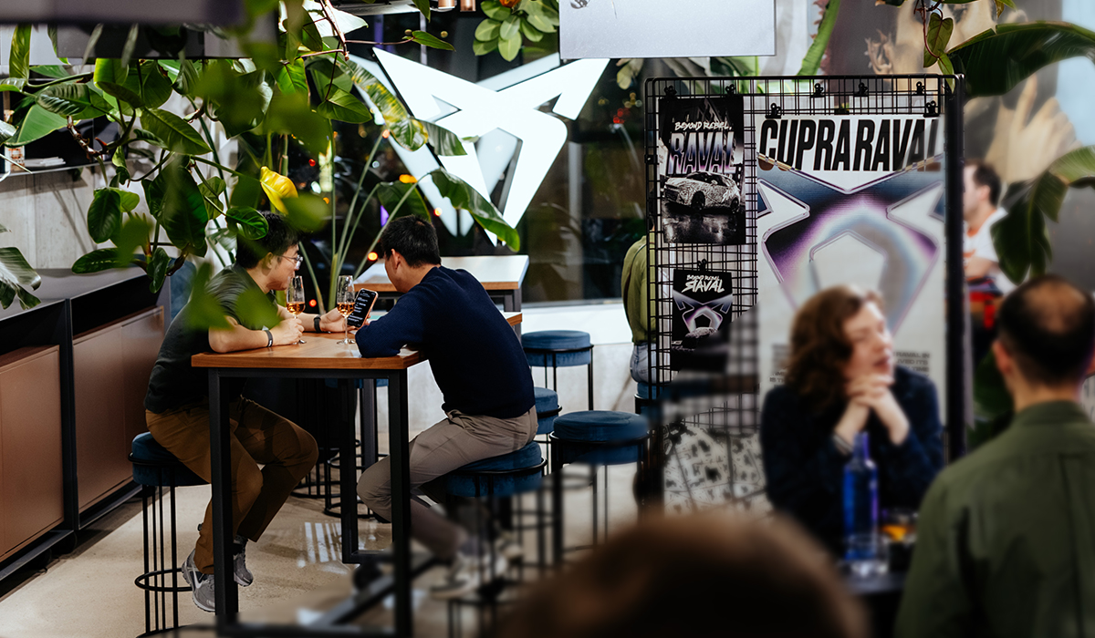 Innenraum des CUPRA Co-Working-Space in Frontperspektive mit Sitzgruppen, Pflanzen und großem Fenster